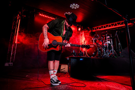 ARD matthews live on stage, bathed in red light, guitar in hand